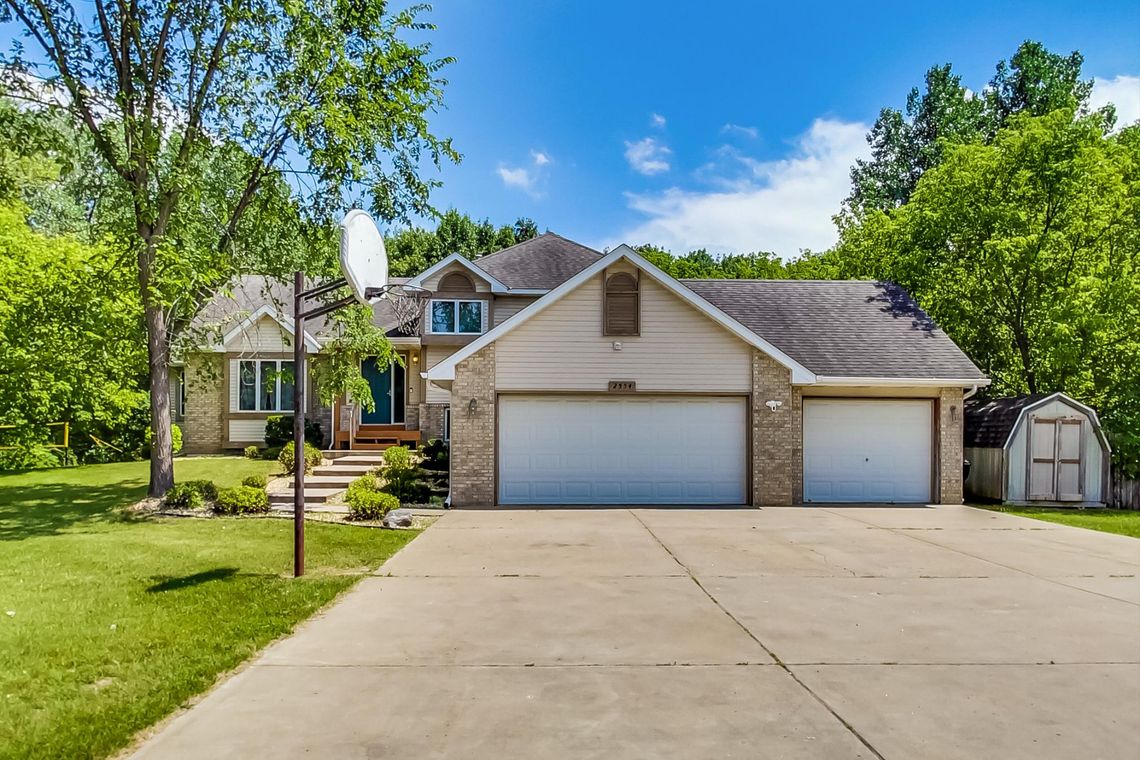 Front of a two-storey home with brick accents, a three-stall garage, wide driveway and basketball hoop.