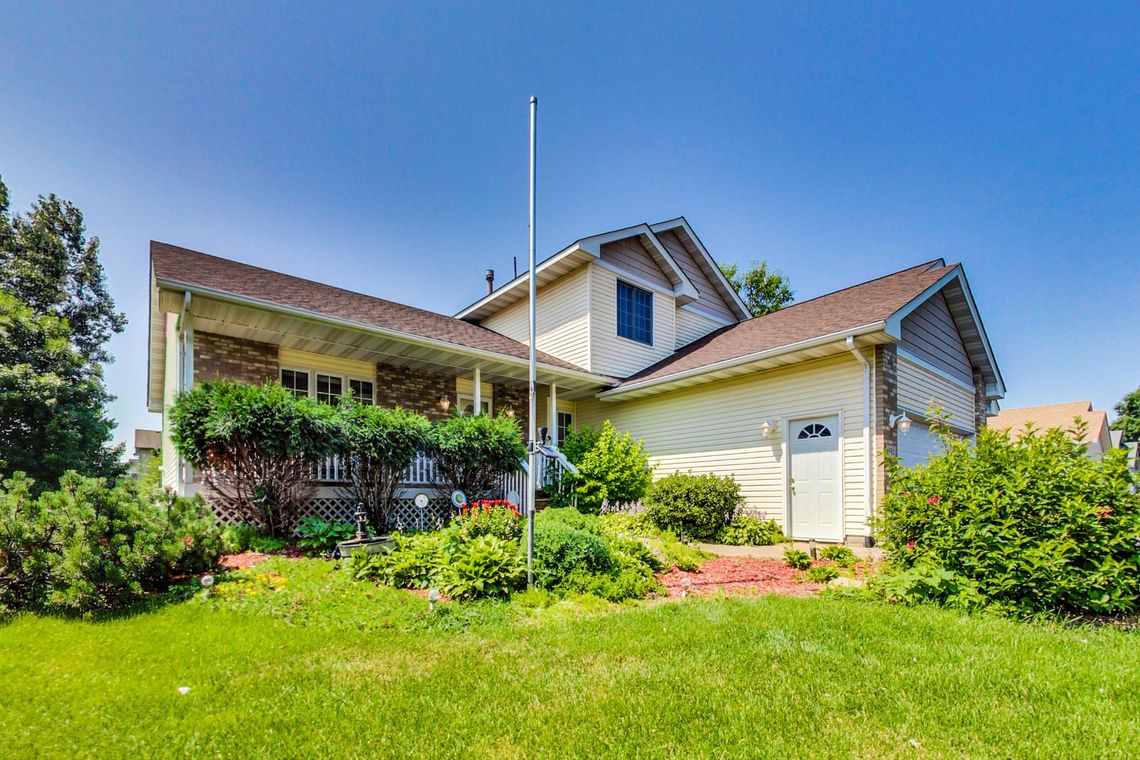 Front of the house with its covered porch, flower beds and a wide summer lawn.