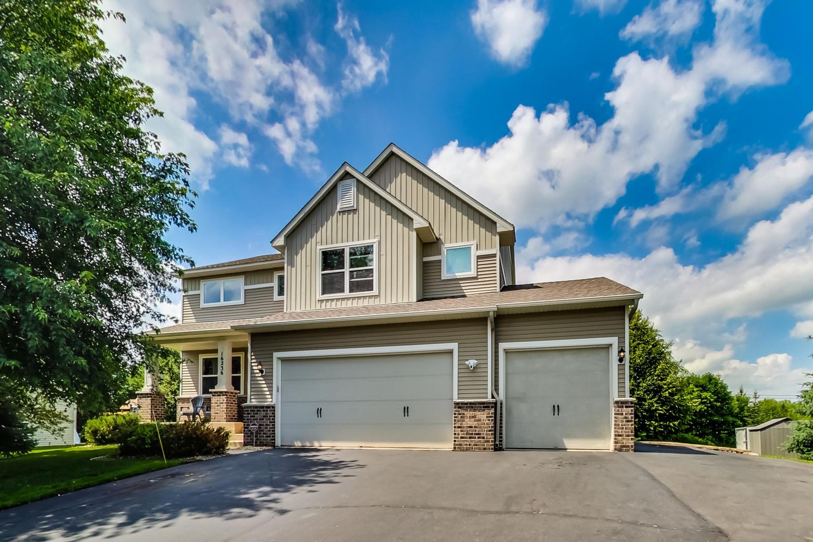 Two-storey house with tan siding, brick trim, a covered front porch and a three-car garage.
